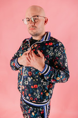 Adult stylish man in multicolored clothes  making heart gesture, sign with hands on his chest. Potrait of funny male person expressing love feelings on pink studio background. Odd bald boy in glasses.