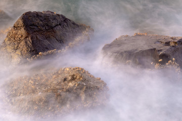Fototapeta na wymiar Misty, moody rocks in the water at sunset - long exposure.