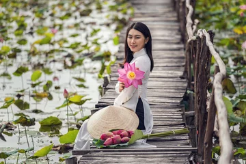 Fotobehang Lotusbloem Portrait of beautiful vietnamese woman with traditional vietnam hat holding the pink lotus sitting on the wooden bridge in big lotus lake, vietnam, aisan or southeast asia travel concept  © THANANIT