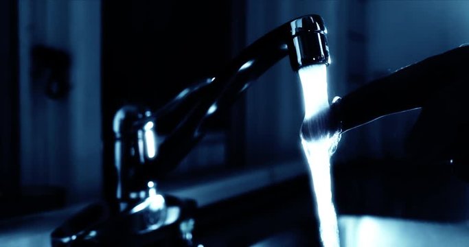 Glass of fresh drinking water. Watertap in kitchen. Person checking temperature with finger before filling a glass of water.