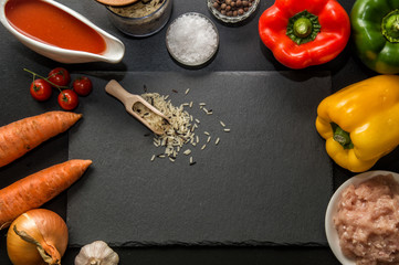 Flat lay, top view. Close up. Ingredients for baking stuffed bell peppers lined around a black stone cutting board. Copy space.