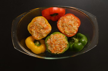 Flat lay, top view. Close up. Cooking a Bulgarian Traditional Dinner. Stuffed bell peppers spread in a transparent pan for baking in the oven. Black background.