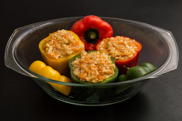 Close up, still life. Stuffed bell peppers spread in a transparent pan for baking in the oven. Black background.