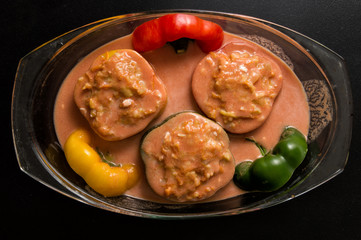 Flat lay, top view. Close up. Cooking a Bulgarian Traditional Dinner. Stuffed bell peppers in tomato sause spread in a transparent pan for baking in the oven. Black background.
