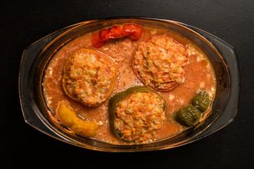 Flat lay, top view. Close up. Cooking a Bulgarian Traditional Dinner. Stuffed bell peppers baked in tomato sauce in a transparent saucepan. Black background.