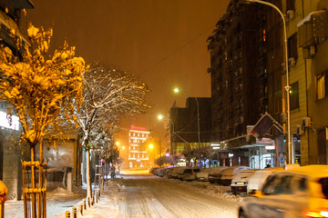 Strong snow fall on street of town in evening. Street covered with snow, and also trees and...
