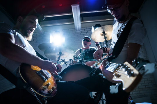 Two guitarists and a drummer play music