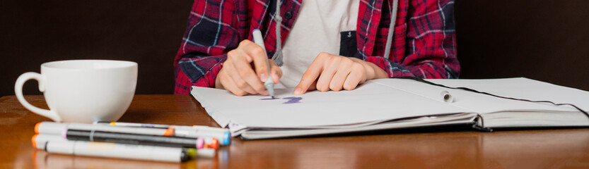 young male sitting at the table and drawing pictures in his notebook with marker b