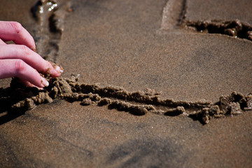 Female fingers touch the heart in the wet sand