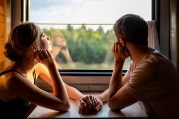 Couple of lovers traveling in train. Mood portrait of romantic pair in wagon looking at window with self reflections in it. Adventure on holiday of happy friends. Man and woman looking at each other.