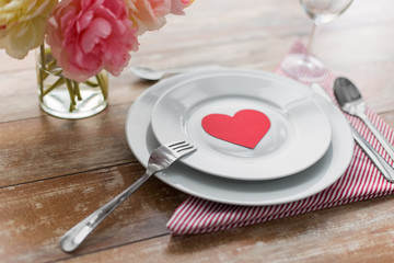 Obraz na płótnie Canvas valentines day, table setting and romantic dinner concept - close up of plates with cutlery, flowers in vase and napkin
