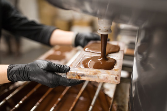 production, cooking and people concept - confectioner filling candy mold with chocolate at confectionery shop