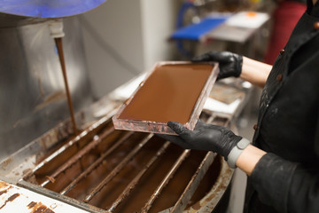 production, cooking and people concept - confectioner filling candy mold with chocolate at confectionery shop