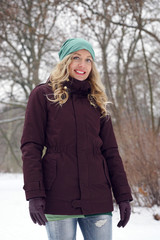 blond woman standing in snow covered woods wearing winter clothes                              