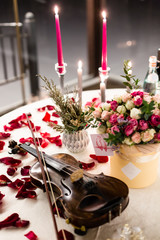 Romantic valentine table setting with wine, dishes, beautiful flowers in box, empty glasses, rose petals, candles, violin