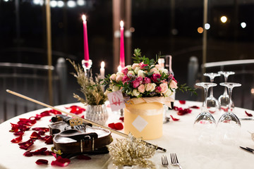 Romantic valentine table setting with wine, dishes, beautiful flowers in box, empty glasses, rose petals, candles, violin