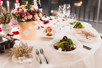 Romantic table setting with wine, beautiful flowers in box, empty glasses, rose petals and candles