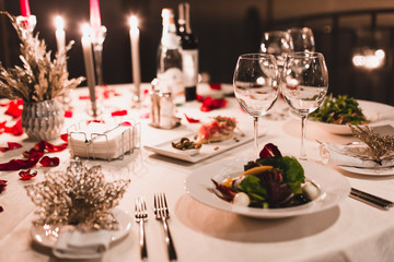 Romantic table setting with wine, beautiful flowers in box, empty glasses, rose petals and candles