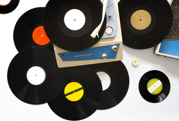 Tocadiscos portable de los años 60 y diferentes discos de vinilo colocados sobre fondo blanco. Cocepto música.