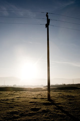 A concrete electricity pylon at sunrise standing alone in a field.