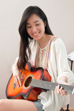 Smiling asian beautiful girl sitting in the music room and playing guitar and leisure concept.