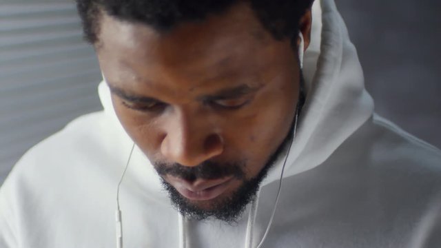 Medium shot of bearded black man in hoodie listening to music with earphones