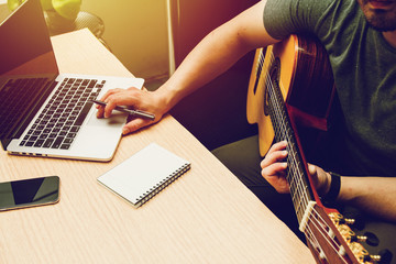 Romantic guitarist Composer or married man writing notes on laptop and playing guitar on black sofa...