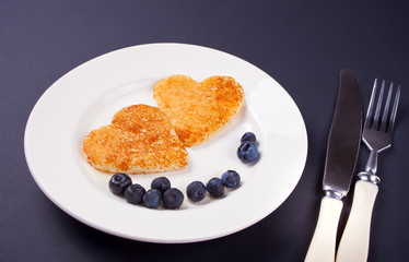 plate of two pancakes in the shape of heart with berries on black table