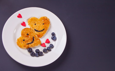 plate of two pancakes in the shape of heart with berries on black table