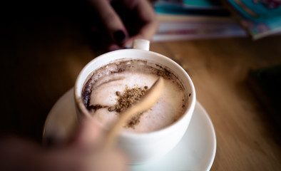 Put sugar in the cup of coffee on wooden table texture ,Close up white coffee cup