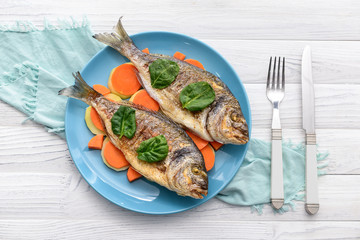 Plate with grilled dorado fish and carrot on white wooden background