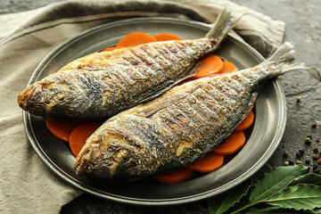 Plate with grilled dorado fish and carrot on grey background, closeup