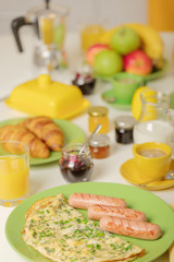 Breakfast time. Omelet with greens and sausages. Croissants and orange juice, jam. Coffee with cream or milk. Fruits - bananas, red and green apples.