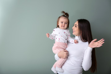 Young woman with her cute little daughter on color background