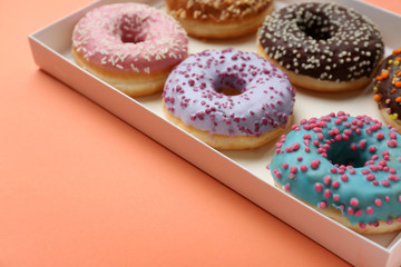 Sweet tasty donuts in box on color background
