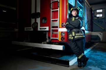 Full-length photo of man firefighter with arms crossed by fire truck