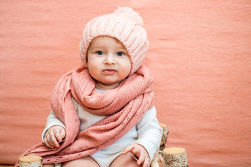 Closeup baby face in snood. Cute baby girl with blue eyes in a pink knitted hat and scarf on a pink background. The concept of a cozy warm winter or spring