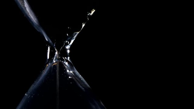 The sand flow in the hourglass with black background and lateral light backlight in lateral composition and possible endless loop