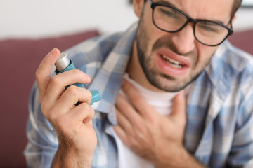 Young man with inhaler having asthma attack at home