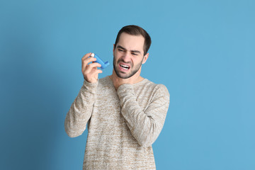 Young man with inhaler having asthma attack on color background