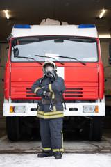 Full-length photo of man fireman in gas mask near fire truck