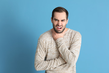 Young man having asthma attack on color background