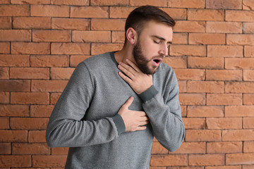 Young man having asthma attack against brick wall