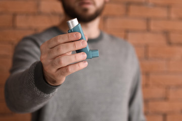 Young man with inhaler against brick wall, closeup