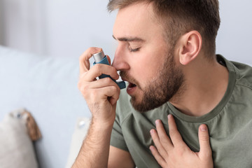 Young man with inhaler having asthma attack at home - obrazy, fototapety, plakaty