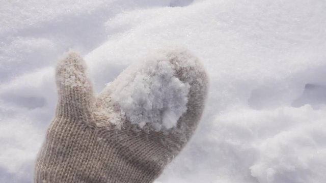 Hand in mitten touches snow
