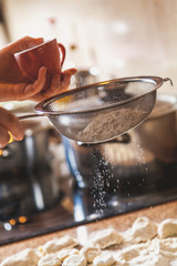female hand holds cup over sieve with flour