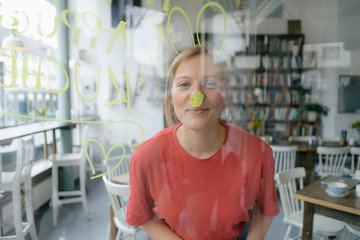 Portrait of smiling young woman posing behind windowpane in a cafe