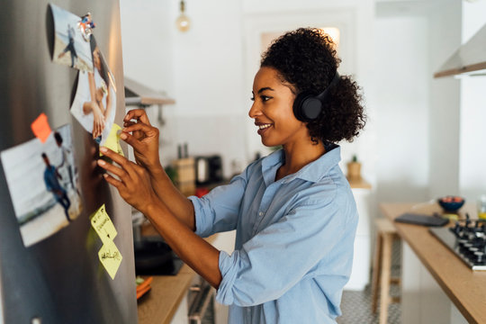 Woman in her kitchen in the morning, posting sticky notes on the fridge