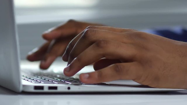 Extreme close up shot of hands of unrecognizable black man working in office and typing on laptop computer keyboard